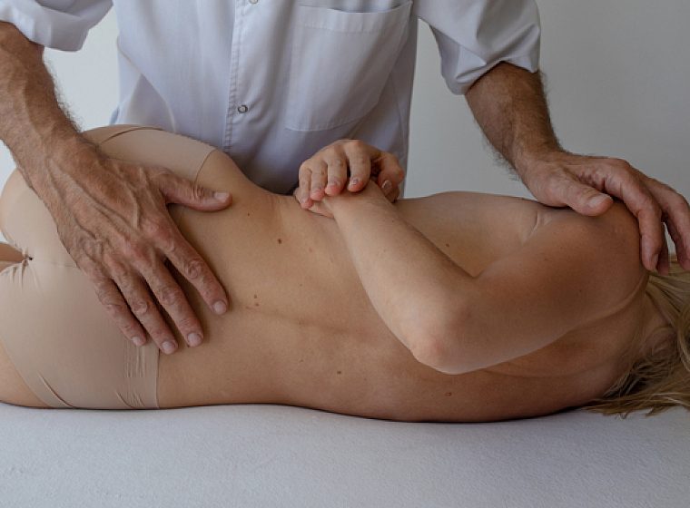 Osteopato rankos ant pacientės nugaros osteopatinio gydymo seanso metu